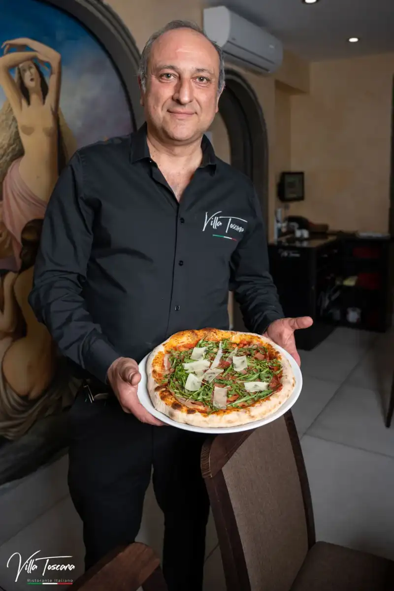 A Villa Toscana chef holding a freshly prepared pizza