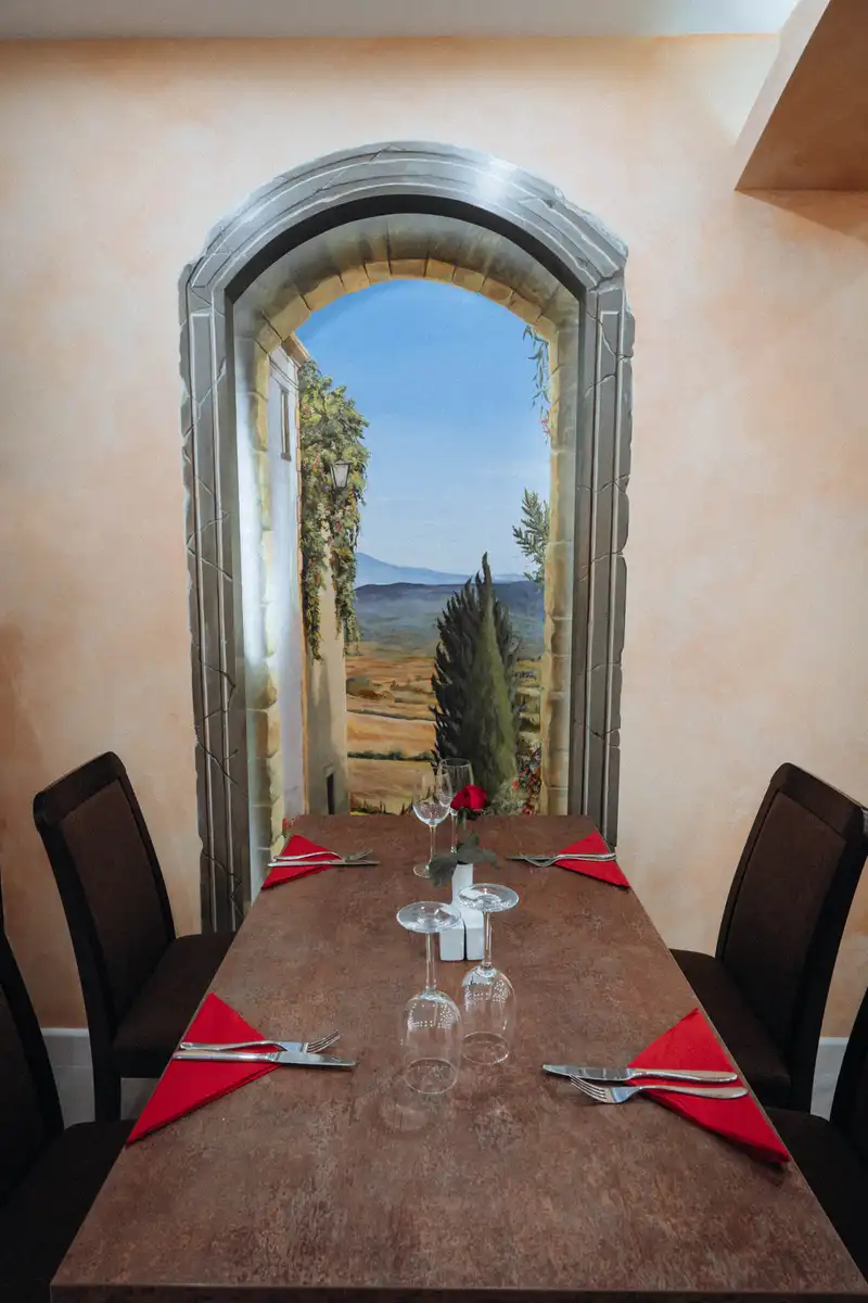 A table for four below an arched painting of the Tuscan countryside