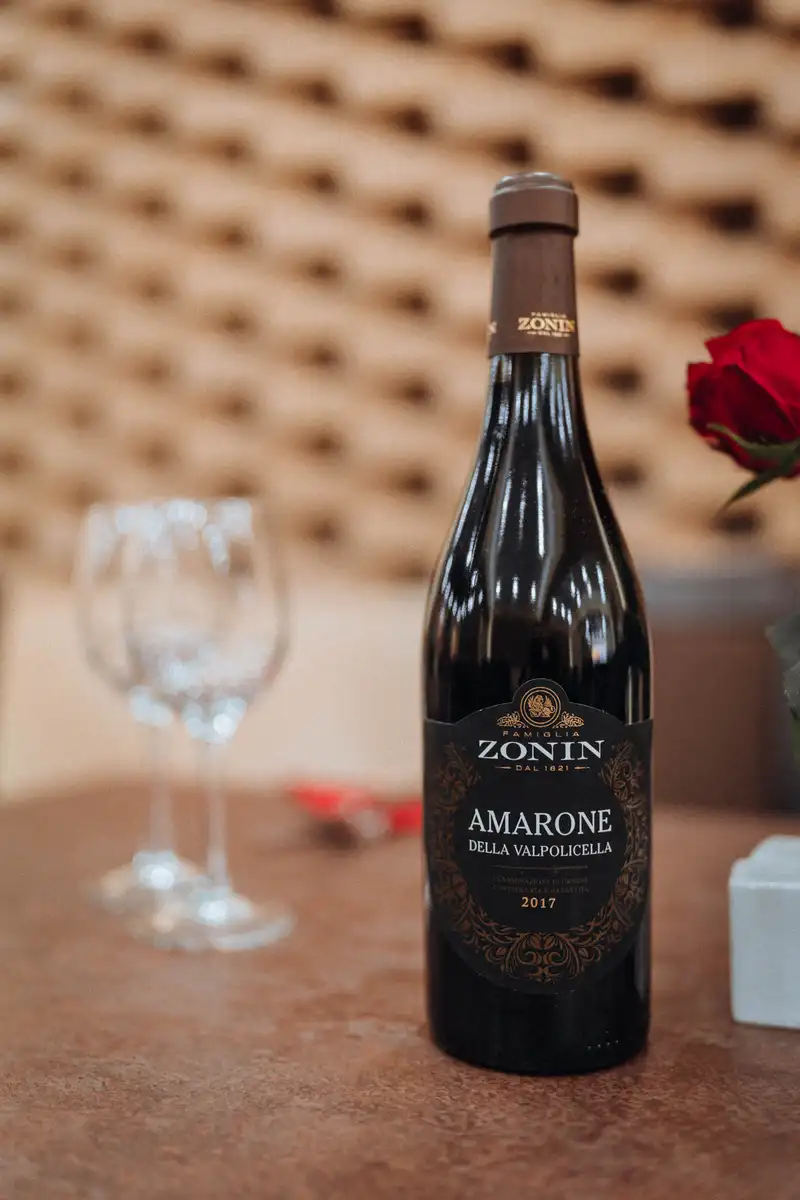 A bottle of red wine and glasses beside a rose on a restaurant table